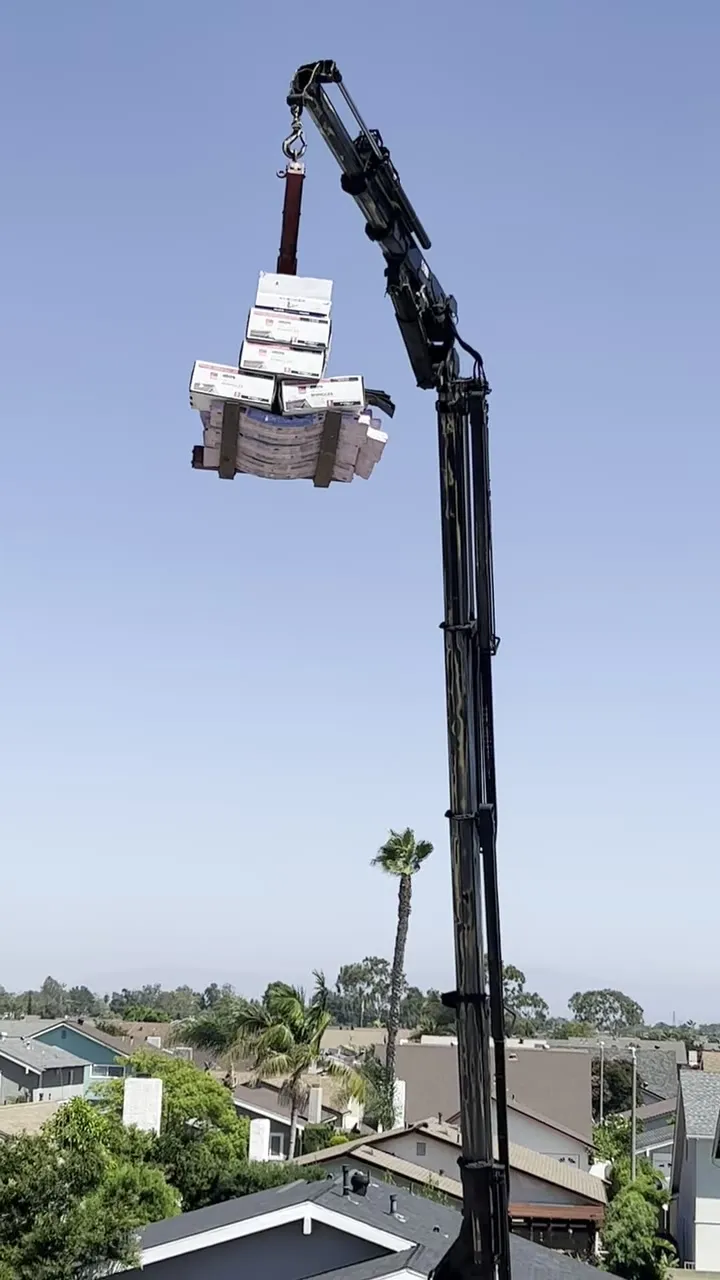 Gancho subiendo una tarima de shingle al techo en un trabajo de Pacific Roofing